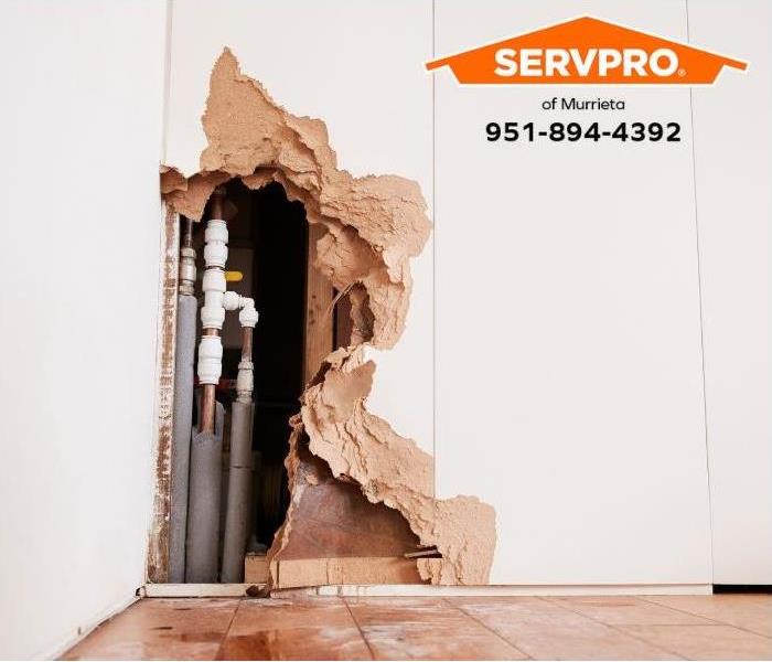 A wall is exposed to reveal burst water pipes and water damage. 