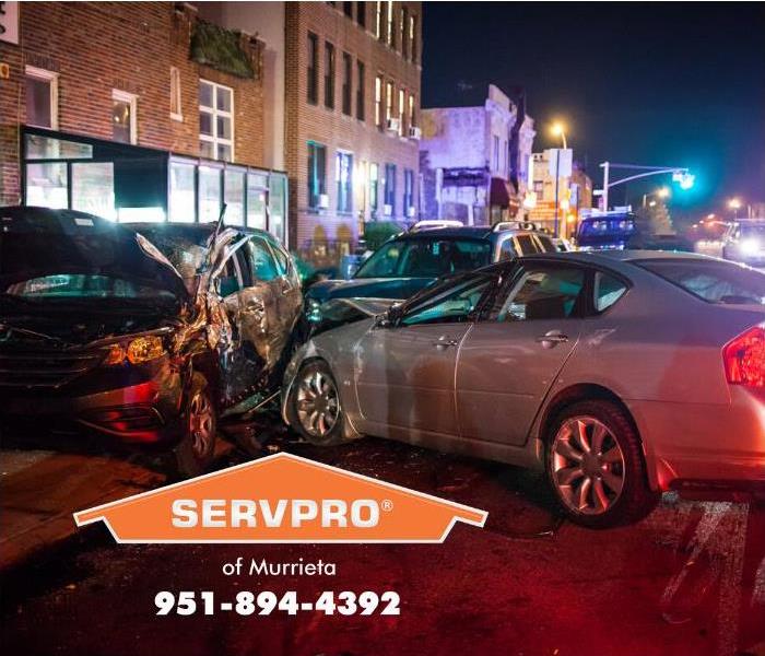 A silver sedan has crashed into a car parked car, pushing the parked car into the side a large brick building, damaging the b